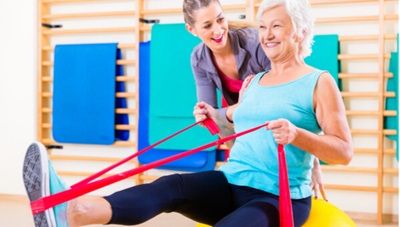 A senior woman is exercising with guidance from a fitness center team member.