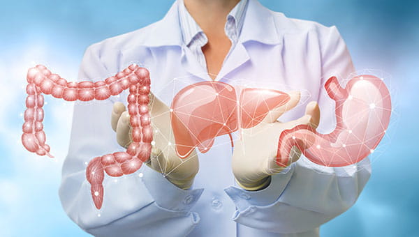 A doctor is standing behind images of a colon, liver and stomach.