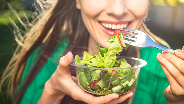 A woman is smiling while eating a salad.