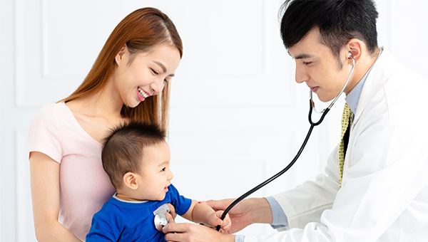 A mother holding her little boy while a male doctor uses a stethoscope to check his vital signs
