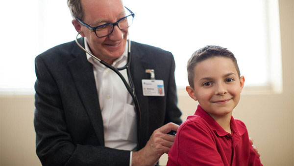 A male doctor uses a stethoscope to check the lungs of a boy patient