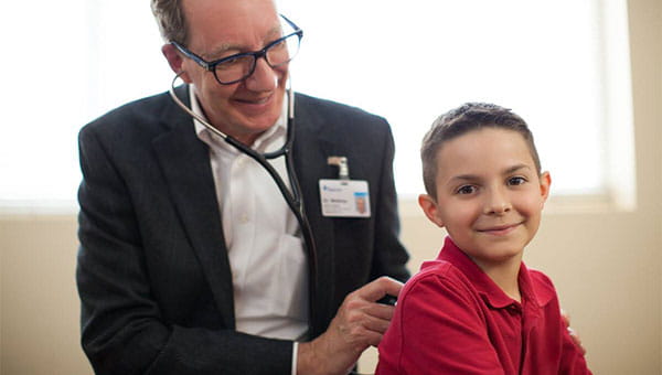 A male doctor uses a stethoscope to check the lungs of a boy patient