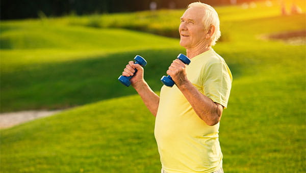 A senior man is lifting weights outside.