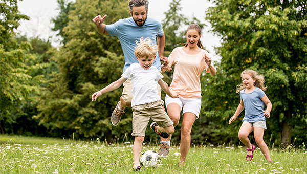 A father and mother playing soccer with their young son and daughter in a park.