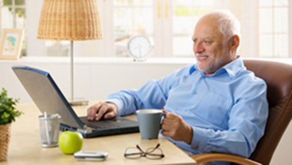 A senior man is sitting at a table and using his laptop computer.