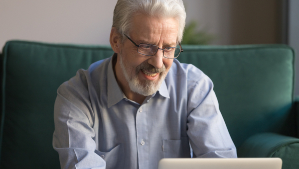 Close up grey haired smiling mature man wearing glasses looking at laptop screen