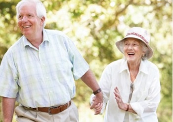 A senior couple is holding hands and walking outdoors.