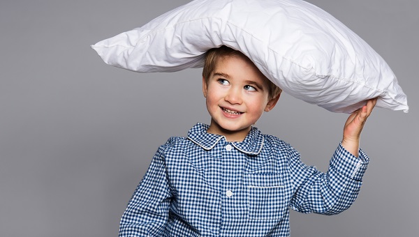 A boy is wearing pajamas and is balancing a pillow on his head.