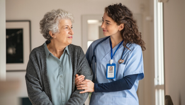 nurse in scrubs helping elderly patient walk