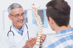 A male doctor talks to a male patient about spine health.