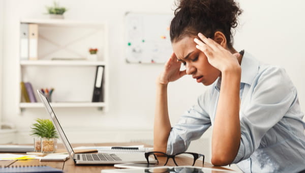 A young woman is visibly distressed while sitting at her desk in front of her laptop.