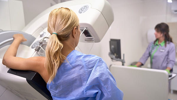 A woman getting a breast scan with a radiology technician working on the background.