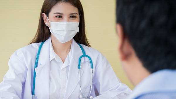 find a cancer specialist card A female doctor is wearing a mask and talking to her male patient.