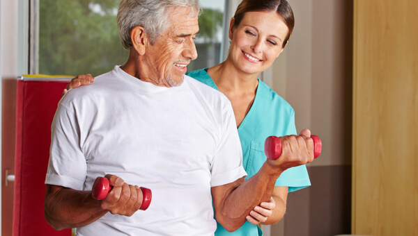 An occupational therapist is helping a senior man build strength in his arms using small weights.