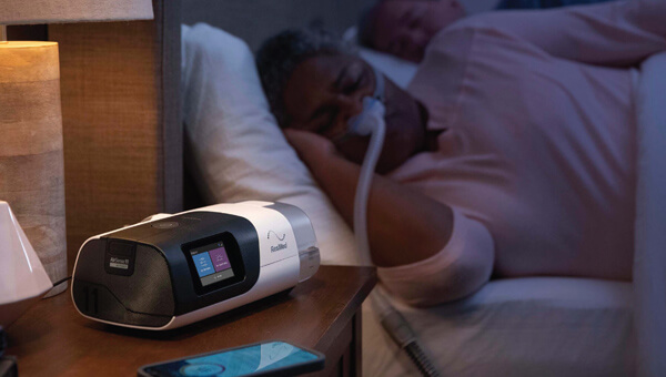 Elderly Black woman sleeping in bed with her partner while connected to a sleep apnea device