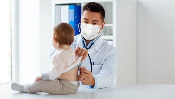 A male pediatrician is wearing a mask while examining a baby in the office.
