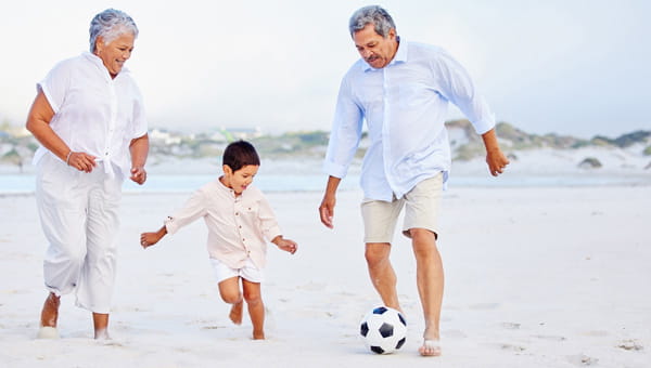 Grandparents smiling and playing soccer with their grandson on the beach