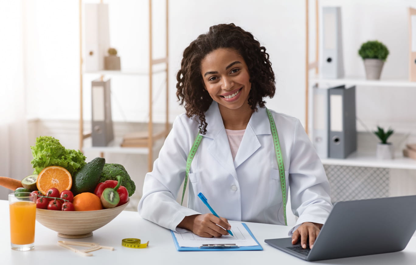 Connect with a BayCare Health Coach Today A woman nutritionist smiling by her desk in a professional setting