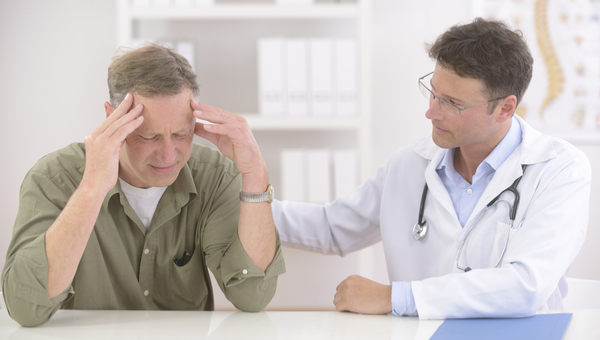 A male doctor talks with a male patient who is in pain.