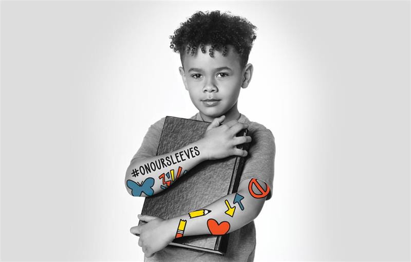 black and white photo of young boy with on our sleeves stickers against blank backdrop