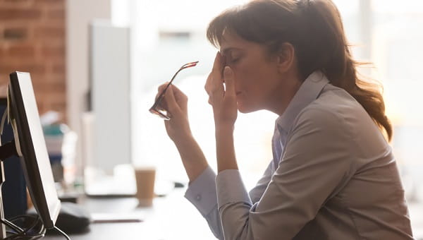 woman at her desk taking off her glasses with her hand on her face
