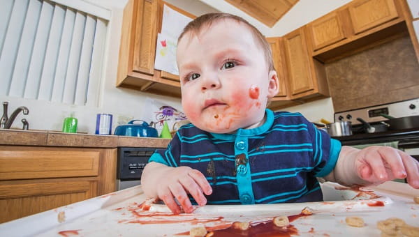 A messy child eats breakfast in the kitchen