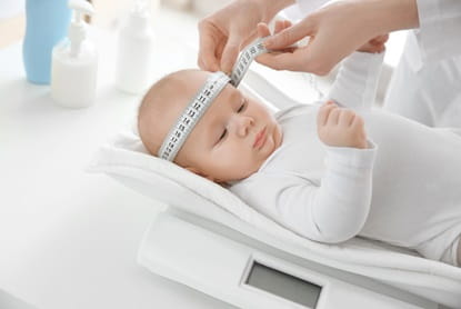 Doctor examining baby on scales in room