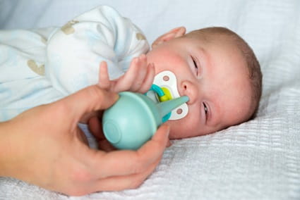 Mother using bulb syringe to clean infant baby's nose