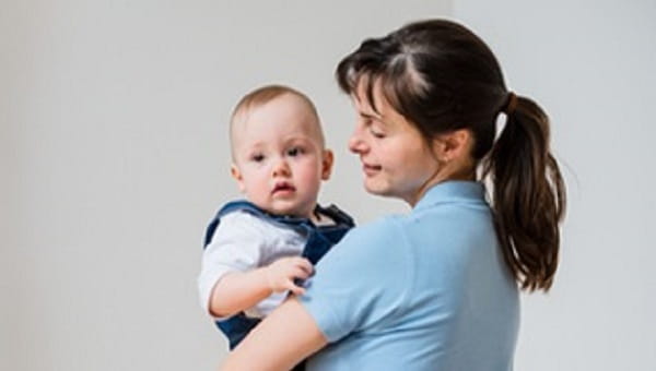 young mother holding her newborn on gray background