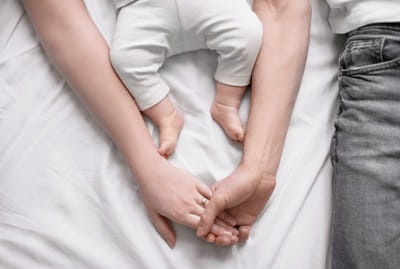 Young parents holding hands together with little baby lying on the bed